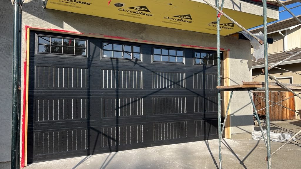 Black carriage-style garage door with window top section on new construction