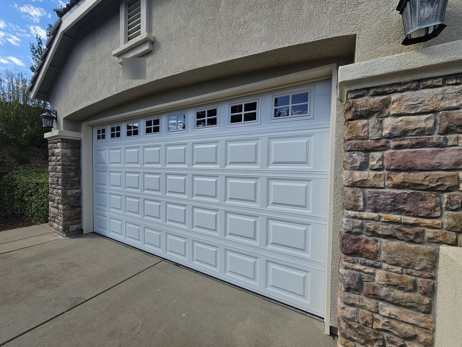 White raised-panel steel garage door with decorative windows and stone columns