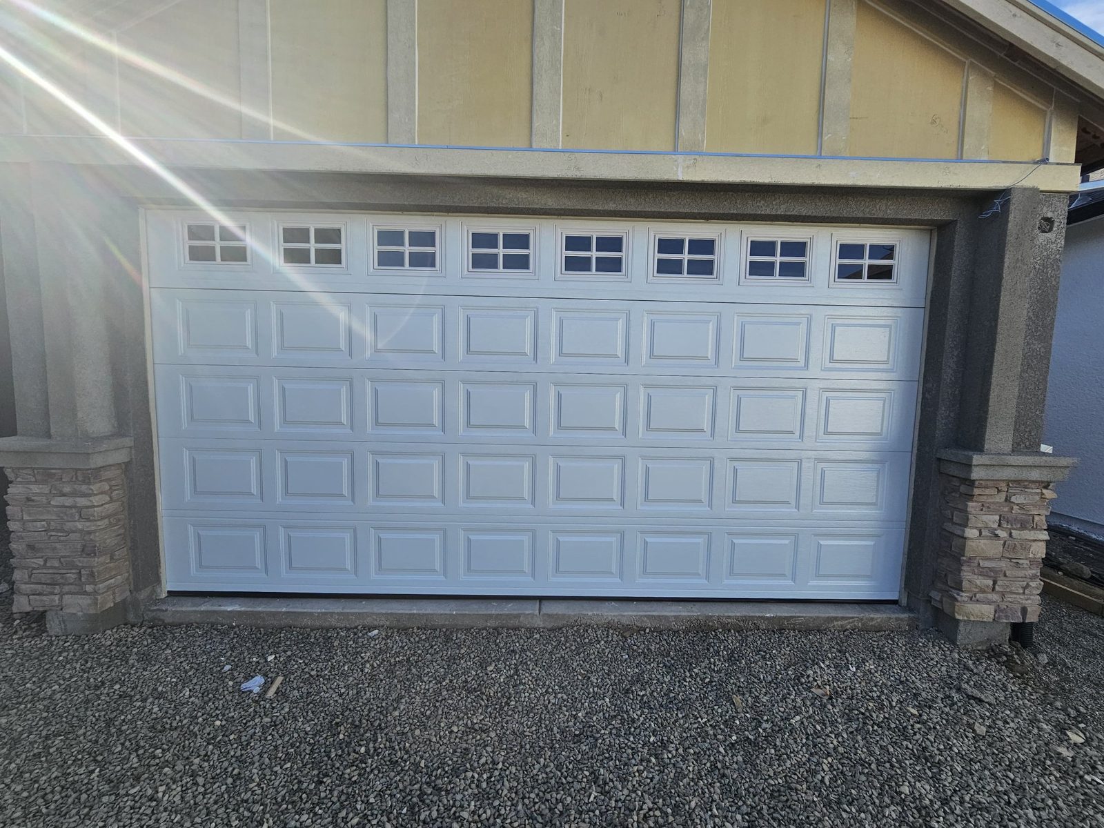 White short-panel garage door with window top section between stone columns