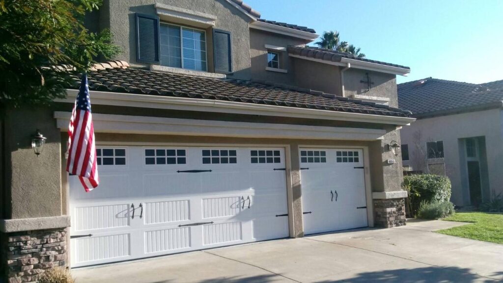 This white garage door exudes elegance and sophistication with its polished, high-quality materials and symmetrical panel design. The simple yet striking hardware adds a touch of understated glamour, resulting in effortless beauty and understated luxury.